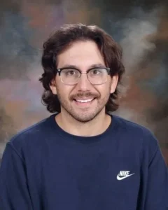 A man with glasses and long hair wearing a blue shirt.